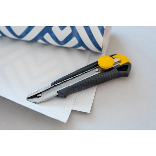 STANLEY 0-10-418 utility knife with black and yellow handle, placed on white paper next to blue patterned roll.