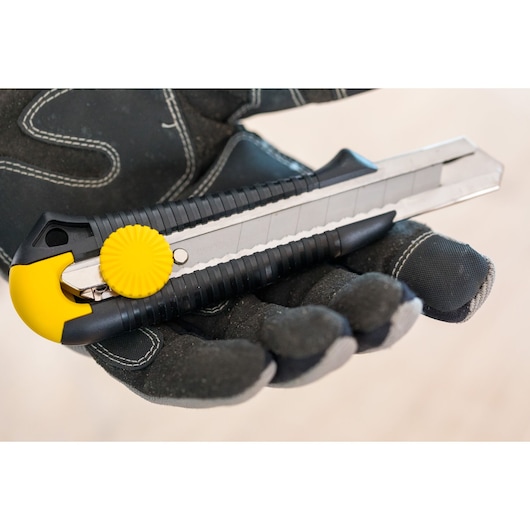 STANLEY 0-10-418 utility knife with yellow lock wheel, held in black work glove, close-up photo.