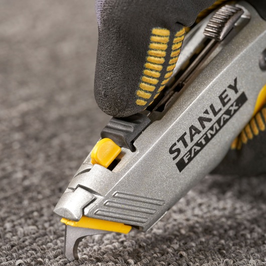 STANLEY 0-10-789 utility knife close-up cutting carpet, silver and yellow handle, gloved hand.