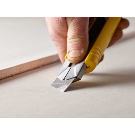 Photo of STANLEY 0-11-725 utility knife cutting drywall, close-up of the blade and yellow handle.