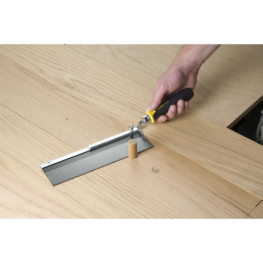 STANLEY 0-15-252 flush cut saw with black and yellow handle trimming a wooden dowel on a light wood surface.