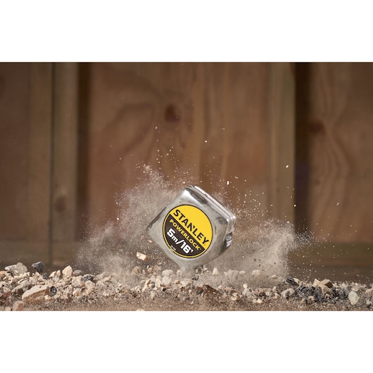 STANLEY 0-33-158 PowerLock tape measure on rocky ground with dust in motion, product photography.