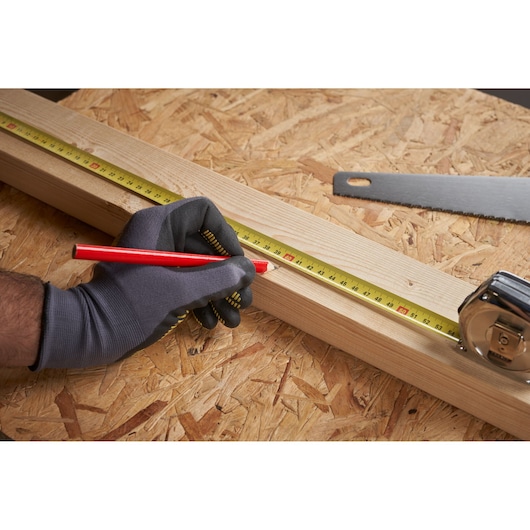 STANLEY 0-33-191 tape measure on wood plank, side angle, gloved hand marking measurements, saw nearby.