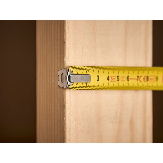 STANLEY 0-33-194 tape measure in use, measuring wooden plank, close-up side angle.