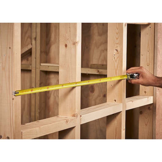 STANLEY 0-33-522 tape measure extended across wooden wall studs, product in use, close-up view.