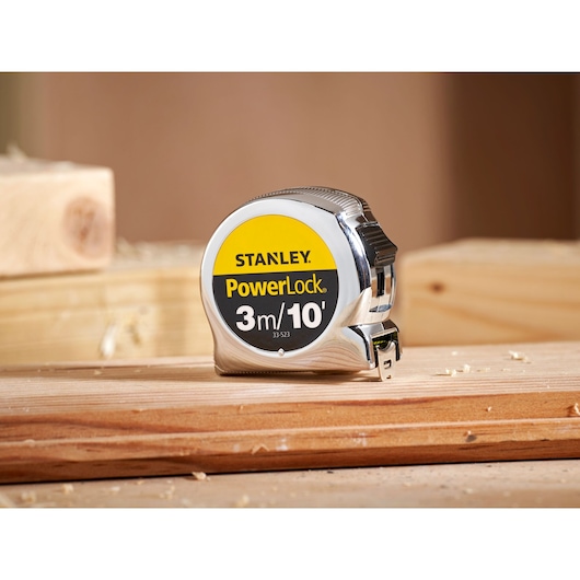 A STANLEY PowerLock measuring tape with a 3 meters / 10 feet length, model 0-33-523, placed on a wooden surface in a workshop setting.