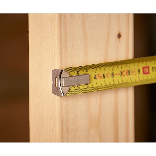 Stanley 0-33-527 tape measure showing yellow blade and metal hook measuring wooden plank, close-up.