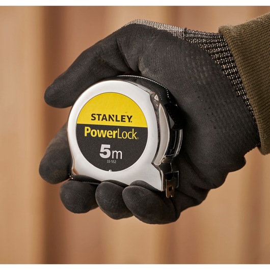 STANLEY 0-33-552 PowerLock 5m tape measure held in a gloved hand, close-up photography.