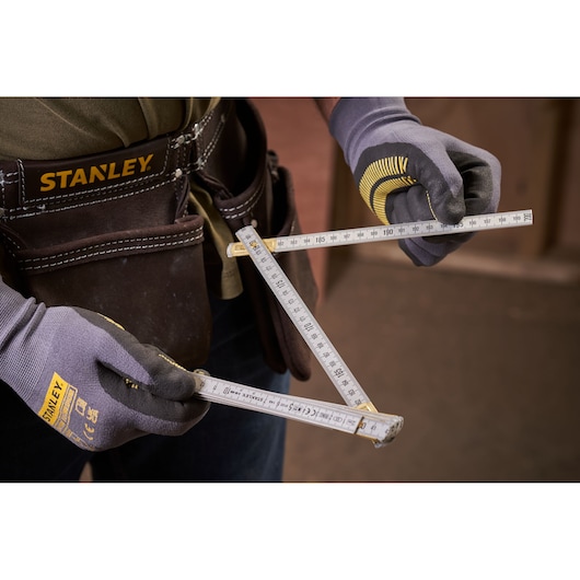 Photo of STANLEY 0-35-305 folding ruler held by gloved hands, worn tool belt visible in background.