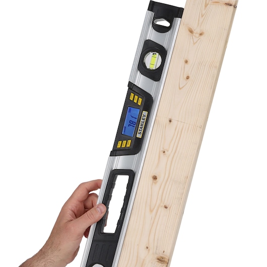 Photo of STANLEY digital spirit level 0-42-065 measuring a wooden plank, close-up of screen and hand holding tool.