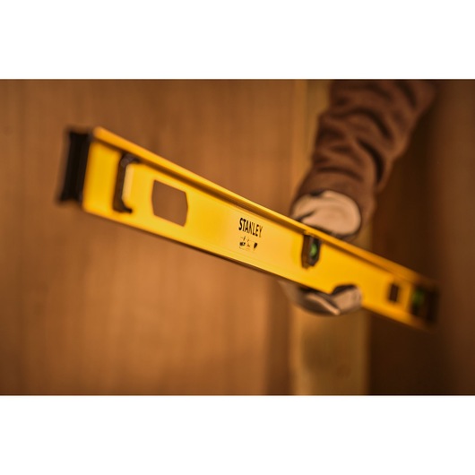 Stanley 0-42-076 yellow spirit level held by gloved hand in construction context, side angle.