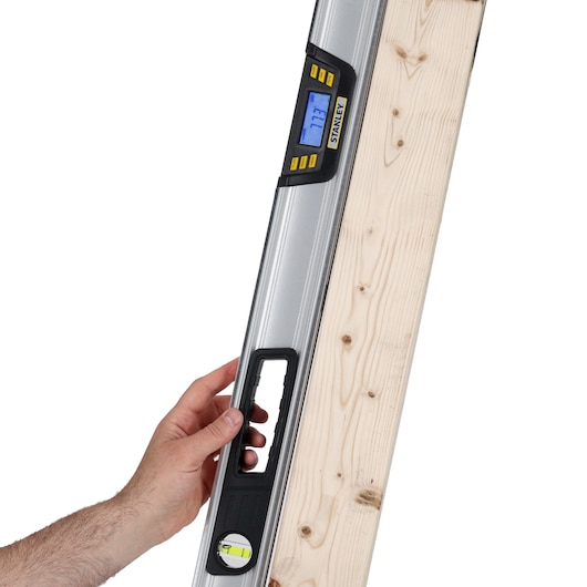 STANLEY 0-42-086 digital spirit level with LCD screen held against a wooden board, close-up view.