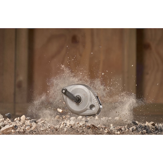 STANLEY 0-47-100 chalk reel photographed in mid-air among dust and gravel, rugged construction site setting.
