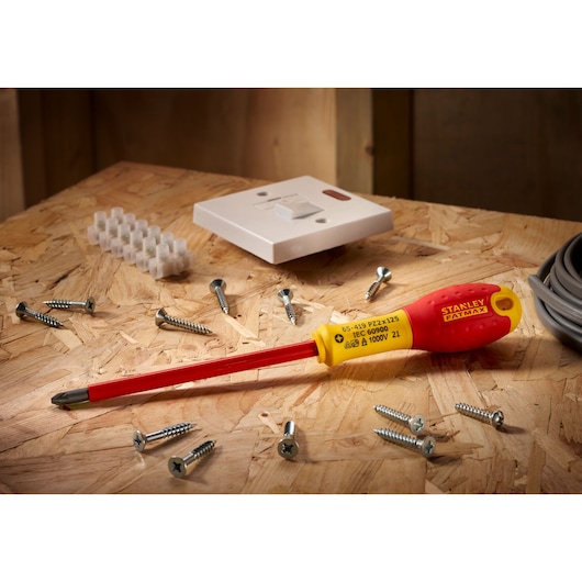 Stanley 0-65-419 insulated screwdriver with yellow and red handle, shown on wooden surface with screws and electrical parts.