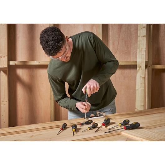 Photo of STANLEY 0-65-437 screwdrivers set on wooden table with worker using one in workshop.