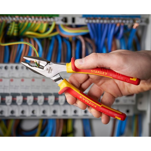 Photo of STANLEY 0-84-001 insulated pliers held by hand near electrical wiring, yellow and red handles.