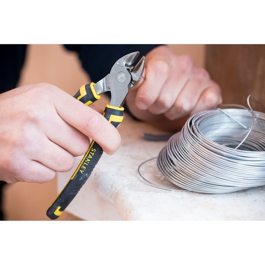 STANLEY 0-89-858 wire cutter pliers used to cut silver wire, close-up with coil on table.