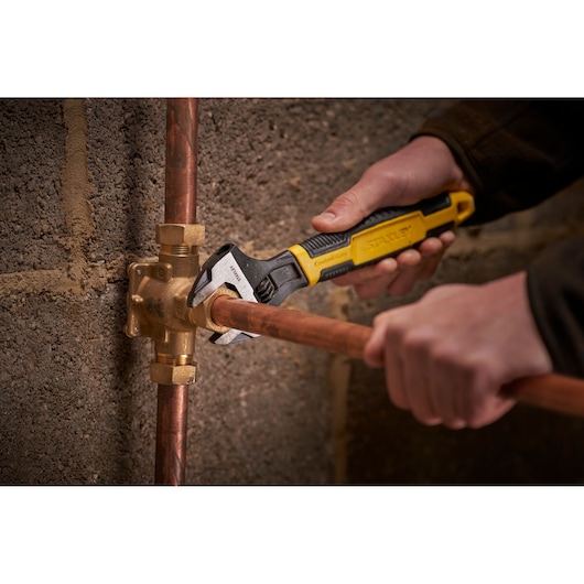 STANLEY 0-90-950 adjustable wrench used on copper plumbing pipes, close-up in a workshop setting.