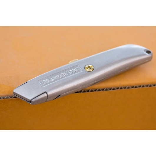 Photo of STANLEY 1-10-099 silver utility knife resting on a cardboard box, angled side view.