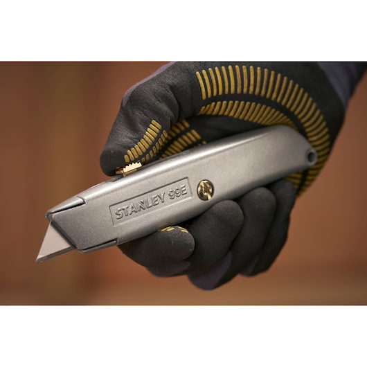 STANLEY 1-10-099 utility knife held in gloved hand, close-up side view, silver metal body.