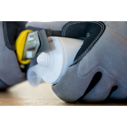 Photo of STANLEY 1-10-425 utility knife cutting plastic tube, close-up with gloved hand, angled view.
