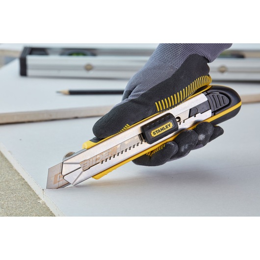 Stanley 1-10-481 utility knife in use, yellow and silver, held by gloved hand cutting drywall.