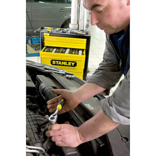 STANLEY 1-13-770 ratchet wrench in use on car engine, yellow STANLEY tool chest in background, workshop scene.