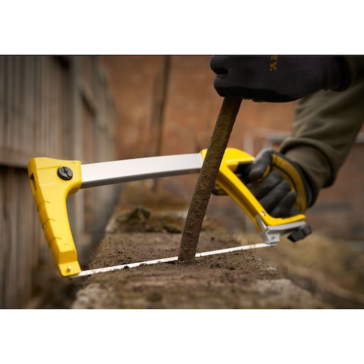 STANLEY 1-20-110 saw in use, cutting a rusty metal rod outdoors, close-up of yellow frame and hand in gloves.