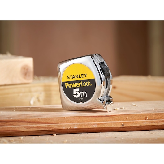 STANLEY 1-33-191 PowerLock 5m tape measure, chrome case, shown on wood, side angle.
