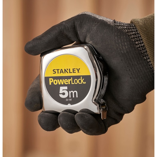 STANLEY 1-33-191 tape measure PowerLock 5m held in a gloved hand, close-up photography.