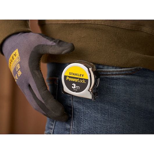 STANLEY 1-33-522 PowerLock 3m tape measure clipped to jeans pocket, person wearing work glove.