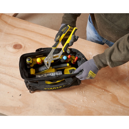 STANLEY 1-93-330 tool bag with yellow-handled pliers on wooden table, photography top view.