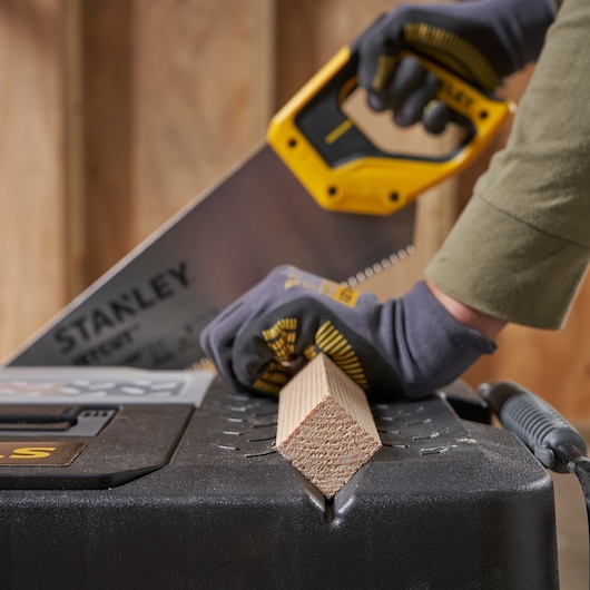STANLEY 1-97-503 saw cutting wood on black toolbox, close-up angle, worker wearing gloves.