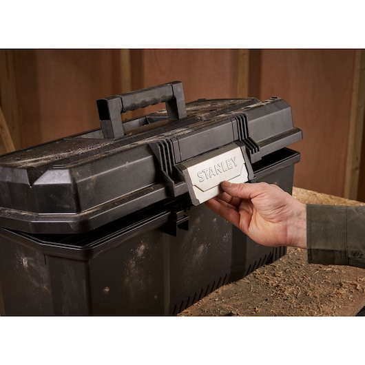 STANLEY 1-97-510 black toolbox with handle, being opened by hand, shown in workshop setting.