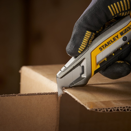 STANLEY 2-11-718 utility knife cutting cardboard, close-up photography, yellow and silver handle.