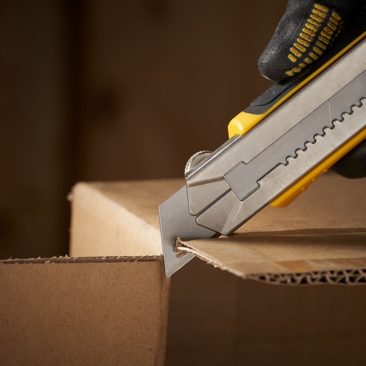 STANLEY 2-11-725 utility knife cutting cardboard, close-up of blade and yellow handle.