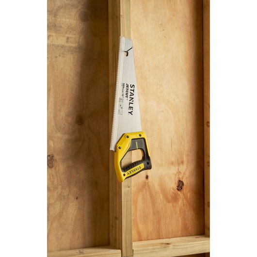 STANLEY 2-15-281 hand saw with yellow handle, angled against wooden beam, product photography.