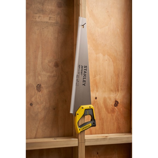 STANLEY 2-15-289 hand saw with yellow and black handle hanging on wooden stud, side angle.