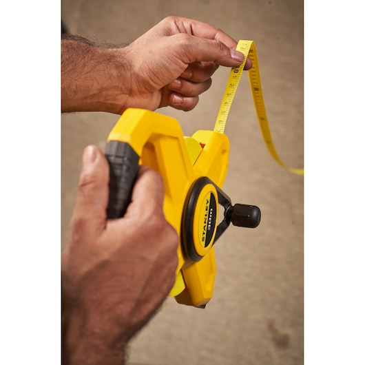 STANLEY 2-34-792 open reel tape measure held in hand, yellow casing, close-up photo.