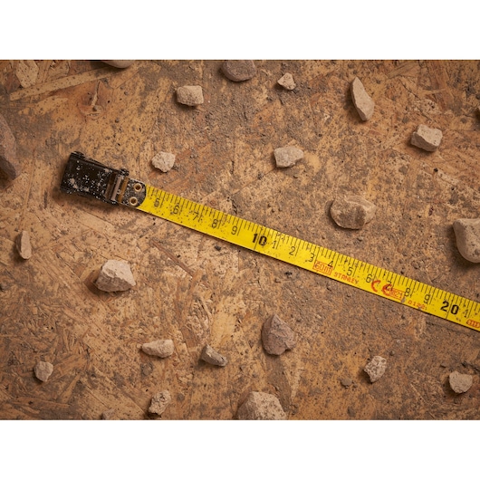 STANLEY 2-34-795 tape measure extended on dusty wood with scattered rocks, top view photography.