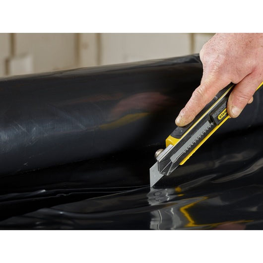 STANLEY 3-11-725 utility knife cutting black plastic sheet, close-up photography.