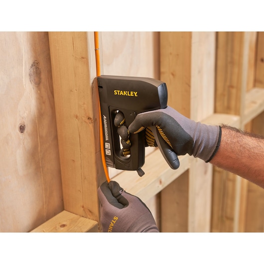Stanley 6-CT-10X stapler tool securing orange cable to wooden frame, close-up view.