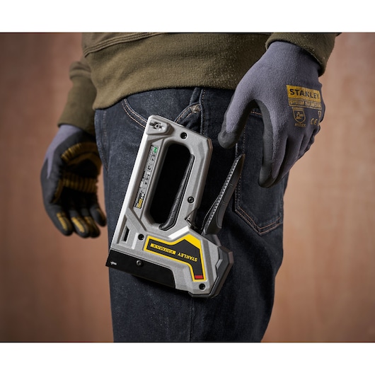 STANLEY 6-TR350 stapler tool held at waist, close-up side angle, worker wearing gloves and jeans