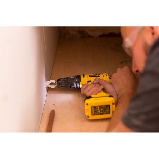STANLEY FMC021S2 cordless drill used horizontally to drive a screw into a wall corner on wood surface.