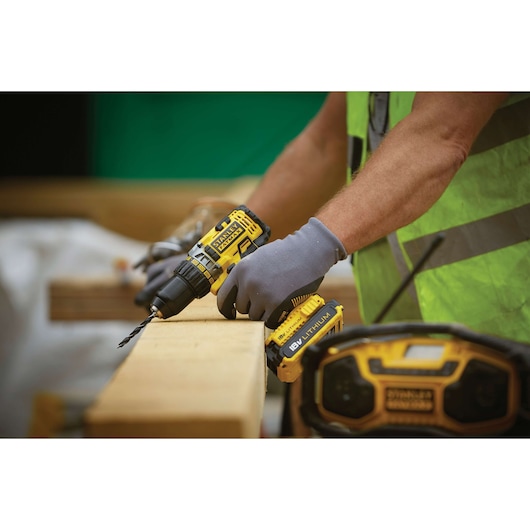 STANLEY FMC600M2S cordless drill in use on wood, yellow and black tool, worker wearing gloves.