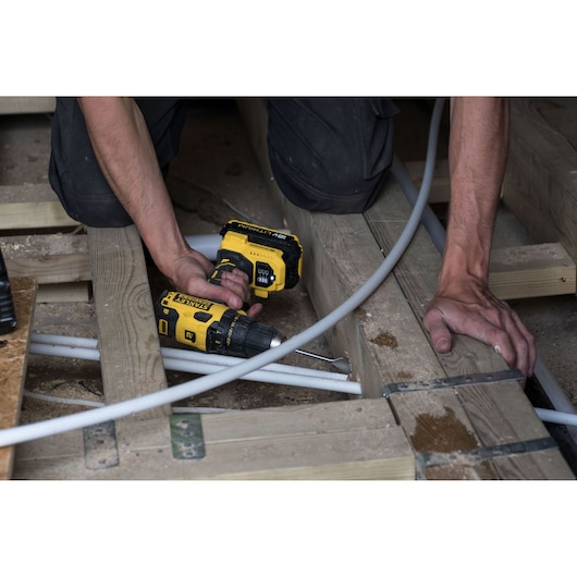 Photo of a worker using a STANLEY FMC607D2 cordless drill on wood beams during construction.