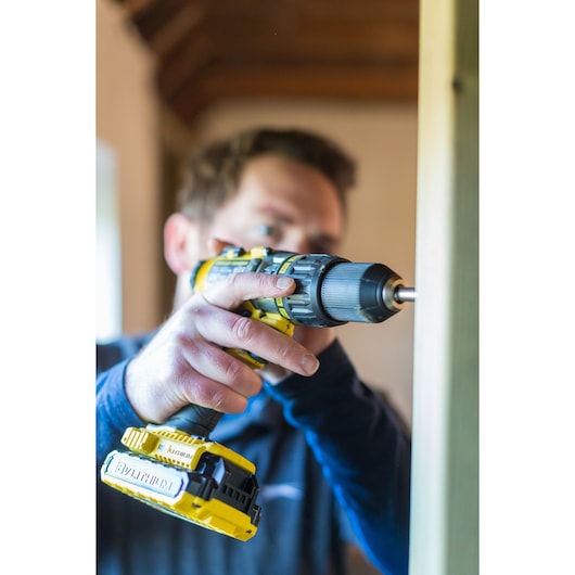 Photo of STANLEY FMC625D2 cordless drill in use, close-up showing yellow and black tool driving screw into wood.