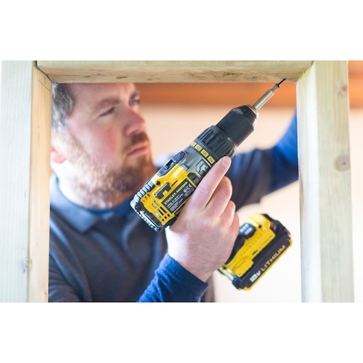 STANLEY FMC625D2 cordless drill in use, yellow and black, drilling into wooden frame, indoor setting.