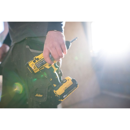 Photo of a person holding a STANLEY FMC625M2S cordless drill driver, yellow and black, construction setting.