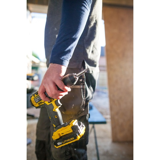 Photo of a person holding a STANLEY FMC625M2S cordless drill with yellow 18V lithium battery in a workshop.